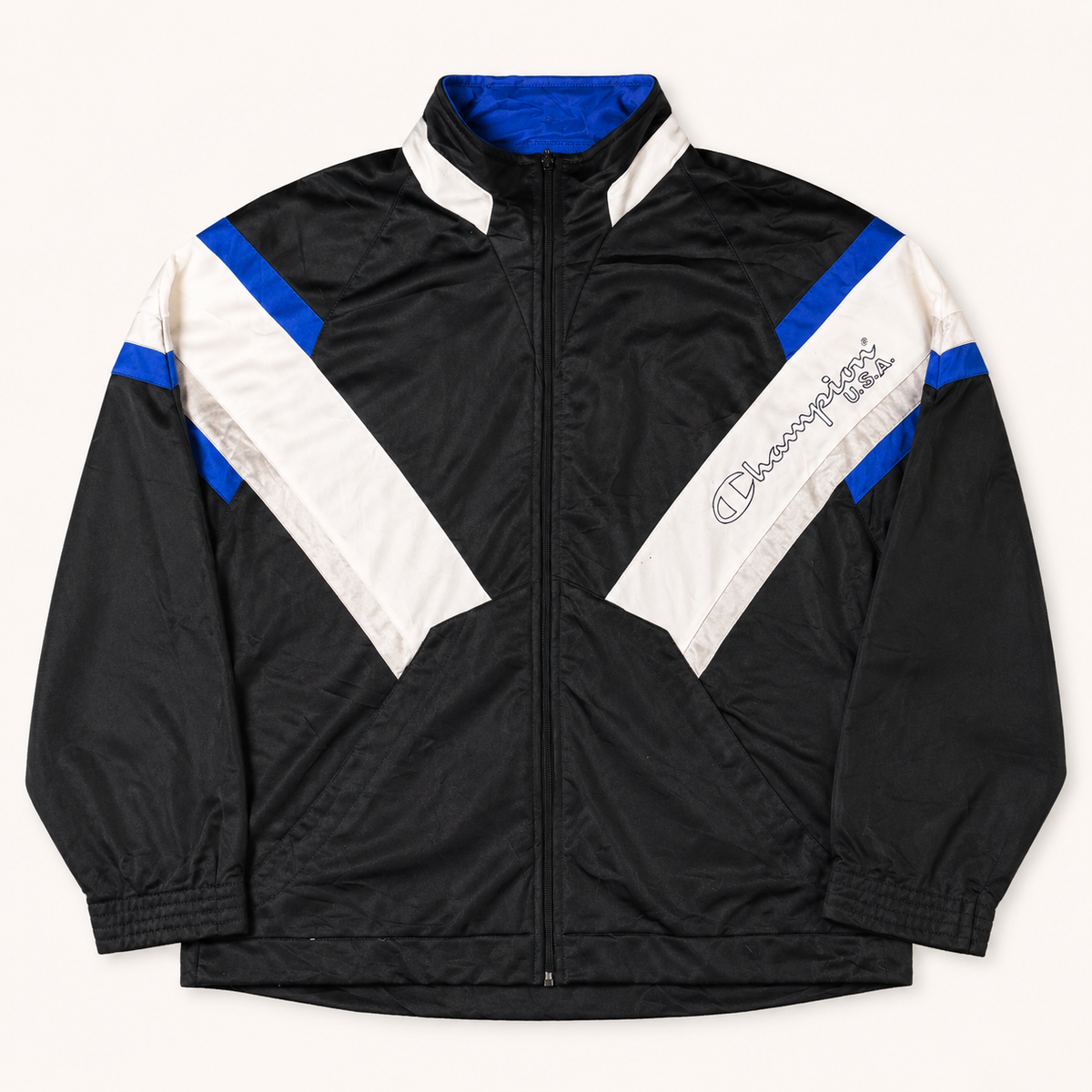 A black Champion windbreaker jacket with white and blue color-blocked panels on the shoulders and sleeves, featuring the signature 'C' logo embroidered on the left chest.